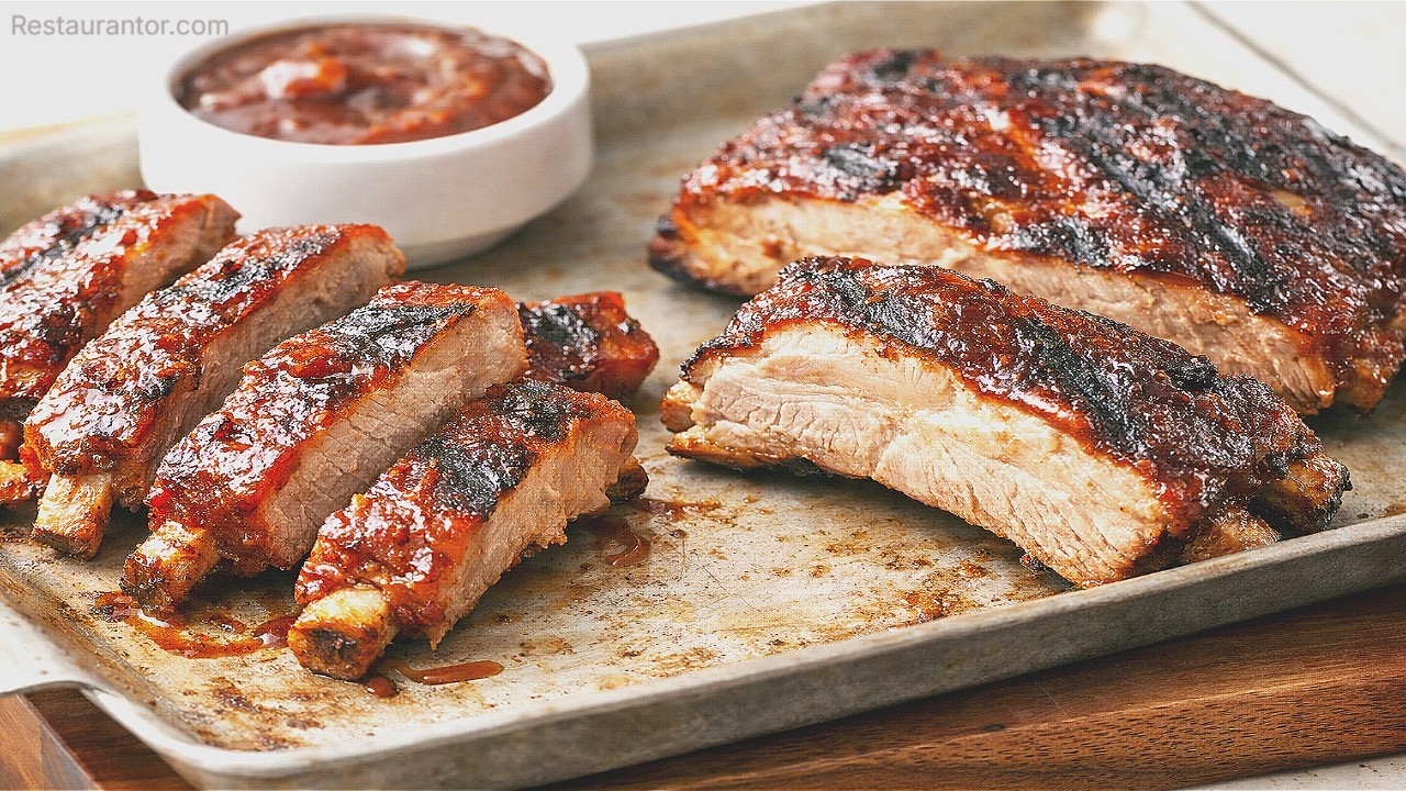 Sticky barbecue ribs on a baking tray with a bowl of BBQ sauce