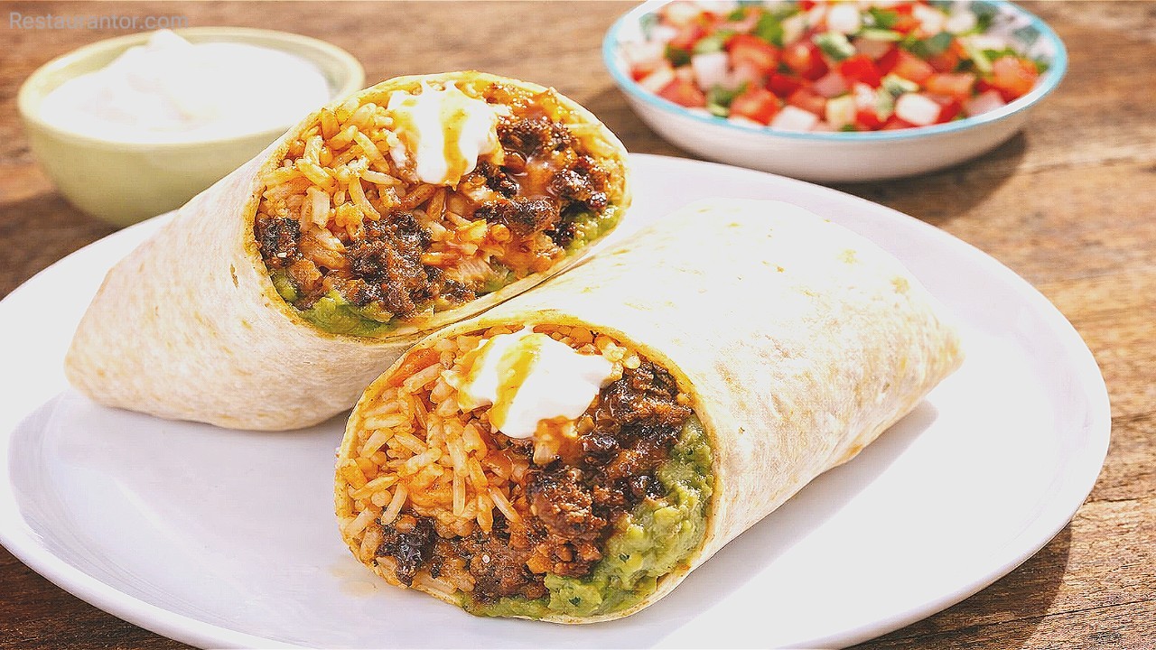 Beef and rice burrito cut in half on a white plate with guacamole and sour cream