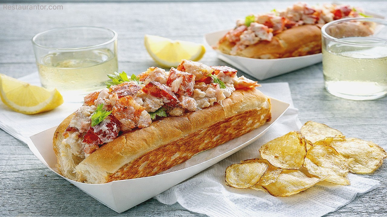 Lobster roll in a toasted bun piled with lobster meat and served with potato chips and lemon wedges